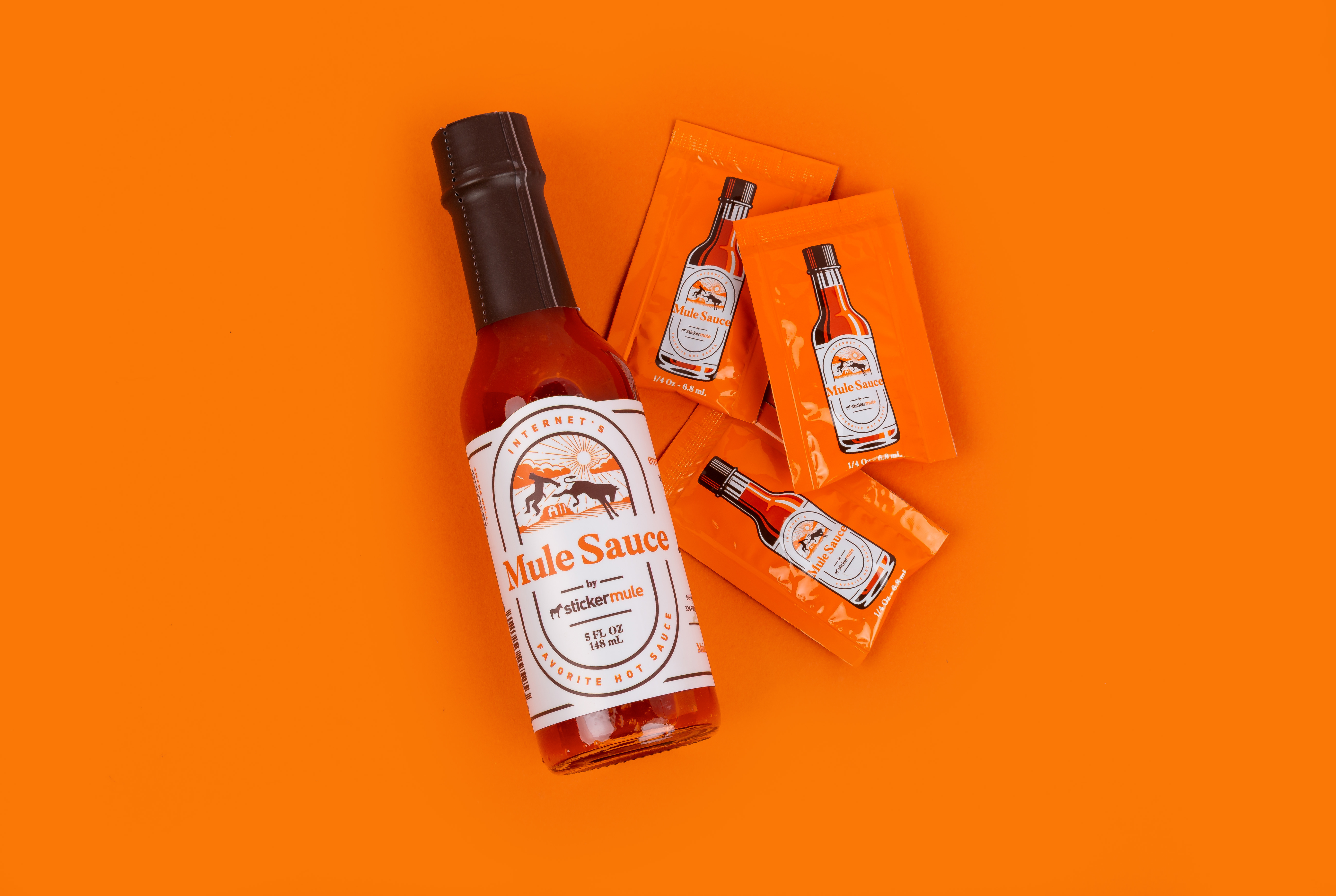 Mule Sauce scharfe Soße Flasche neben Mule Sauce Päckchen auf orangefarbenem Hintergrund