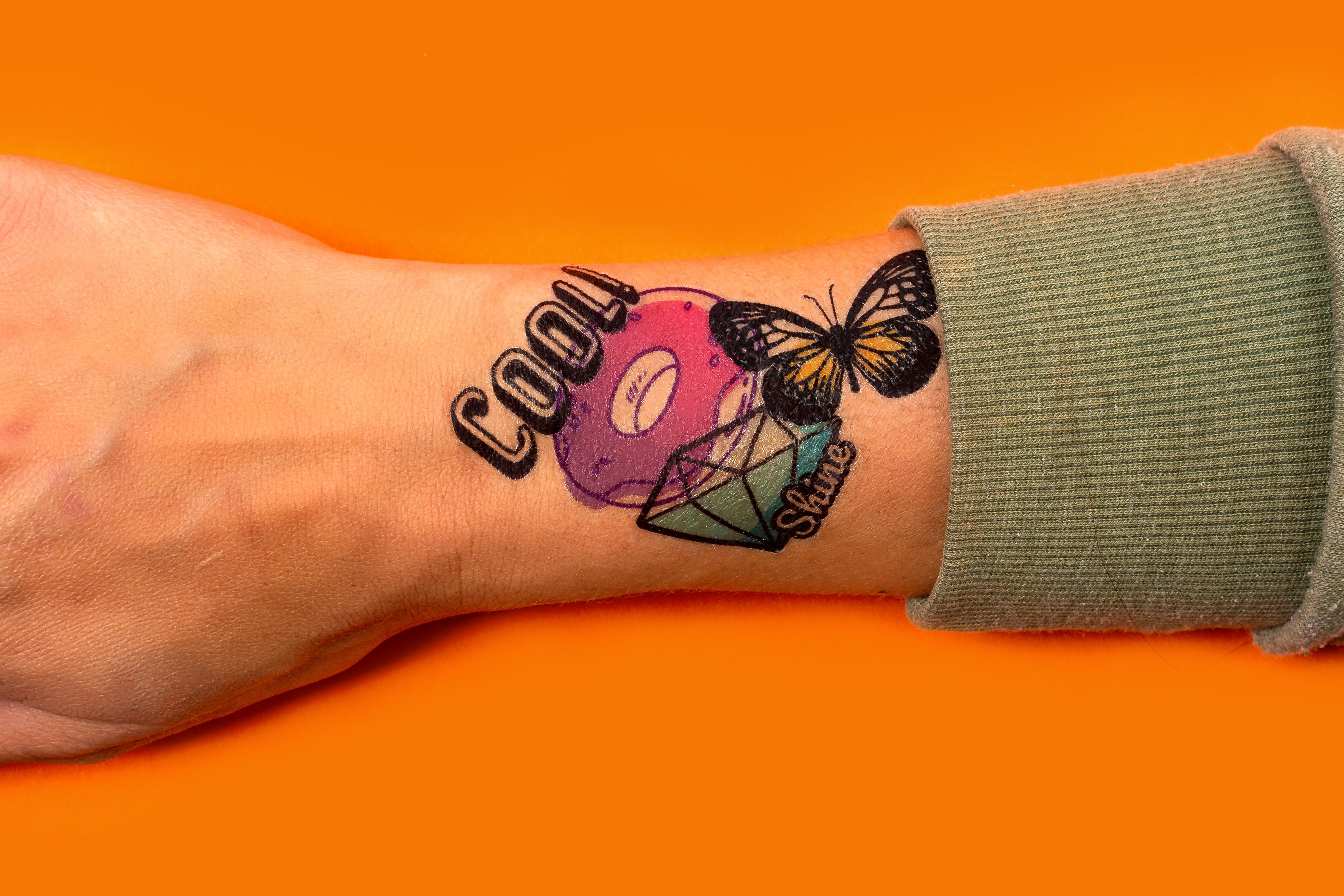 person's wrist with four temporary tattoos layered on top of each other on over an orange background