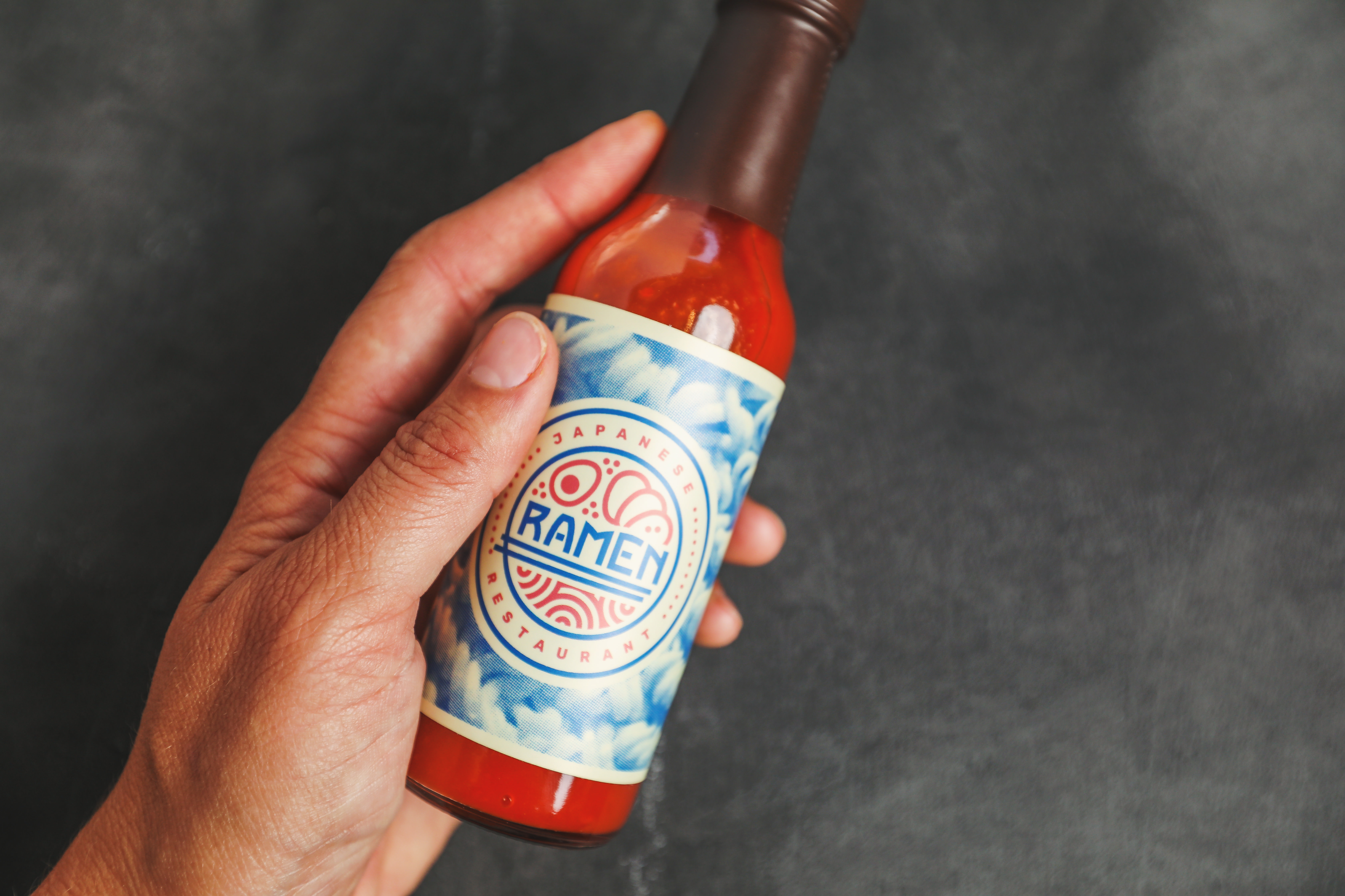 hand holding a bottle of white label hot sauce with brand name ramen on the label